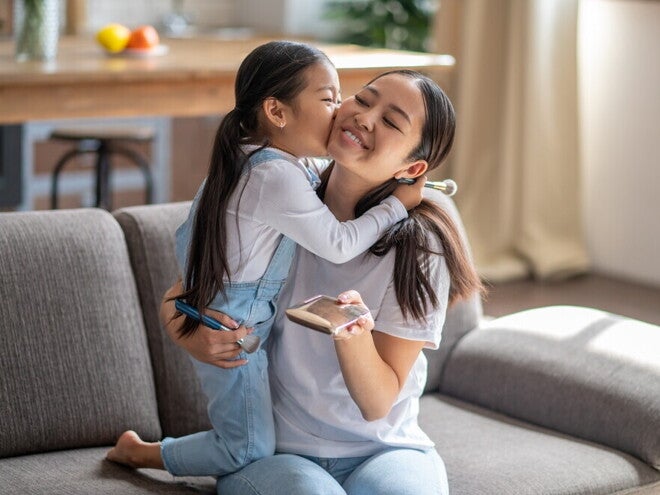 Know Your Solo Parent Benefits in the Philippines Preschool-age child kisses her mom, a solo parent, while they’re in the living room.