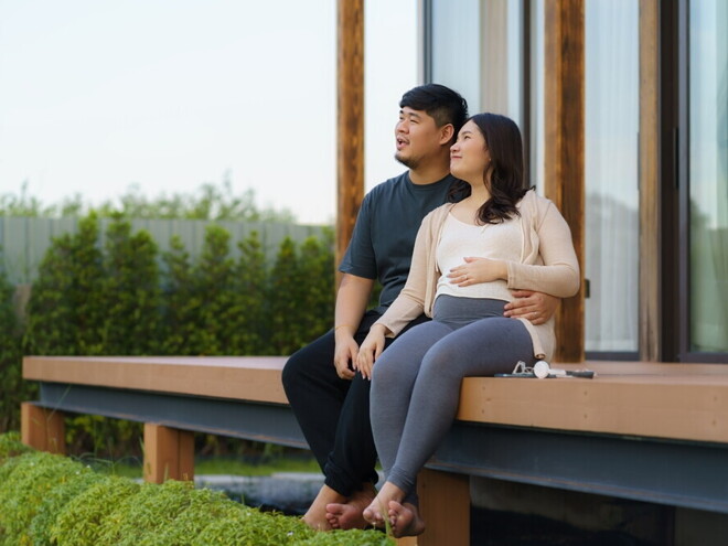 Asian pregnant couple sit on the porch of their vacation home during their babymoon