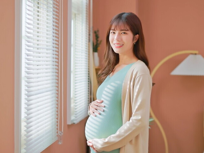 Asian woman, who is 39 weeks pregnant, holds her belly bump and smiles at the camera. Asian woman, who is 39 weeks pregnant, holds her belly bump and smiles at the camera.