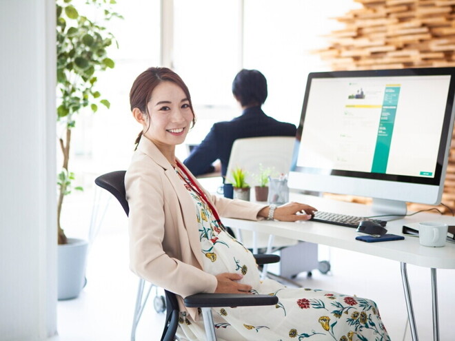Pregnant Asian takes a break from working on her computer at an office.