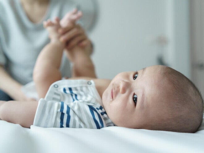 A young Asian mother changing her baby's diaper on a bed.