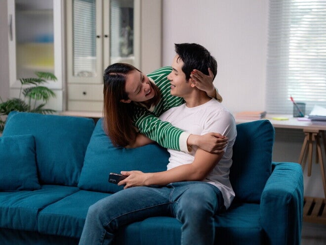 Young Asian couple hugging each other on the sofa and discussing the answer to: what is family planning?