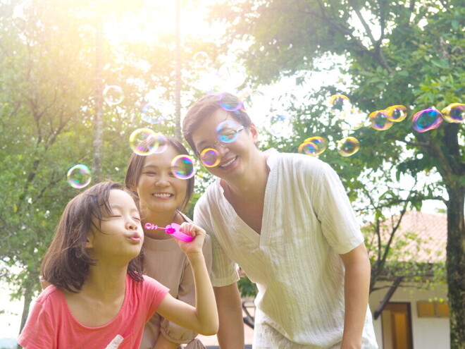 Header_Image Filipino parents watch their daughter blow bubbles during a hot day.
