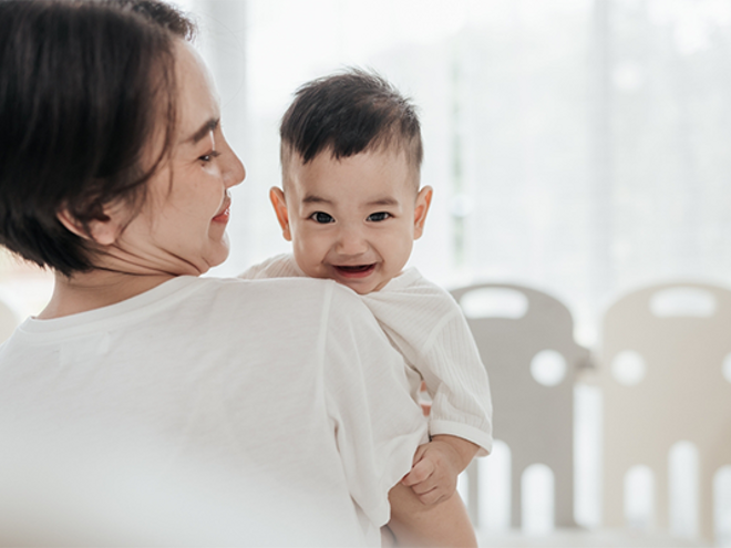 Smiling Asian mom with her laughing baby enjoys the early childhood stage