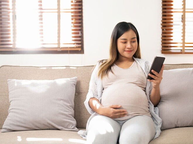 Smiling Asian pregnant woman who is 38 weeks pregnant checks her phone Smiling Asian pregnant woman who is 38 weeks pregnant checks her phone
