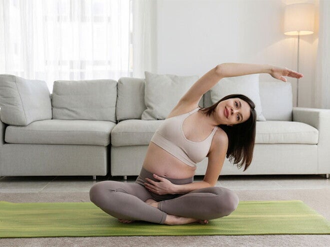 Smiling Asian pregnant woman who is 9 weeks pregnant performs yoga at home Smiling Asian pregnant woman who is 9 weeks pregnant performs yoga at home