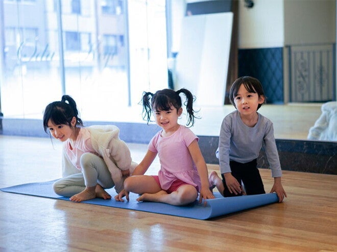 Three Adorable Asian preschoolers with healthy tummies sit on a yoga mat in fitness studio