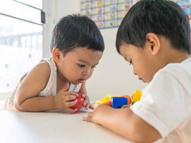 Asian toddler intently stares at the toy of another child.