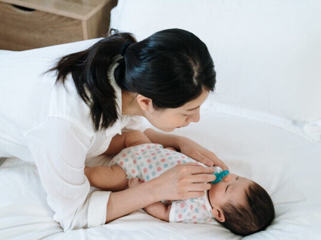 Asian mom giving pacifier to little Asian newborn.