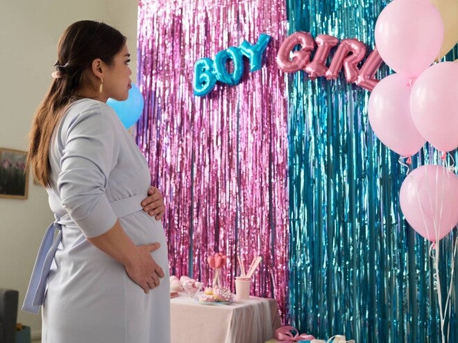 Young pregnant Asian looking at streamers during a gender reveal party.