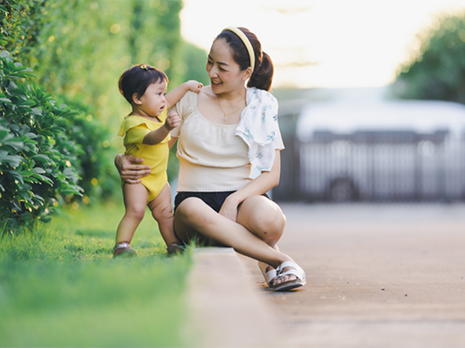 Young Asian mom supports her baby who's practicing their motor skills while outdoors. Young Asian mom supports her baby who's practicing their motor skills while outdoors.