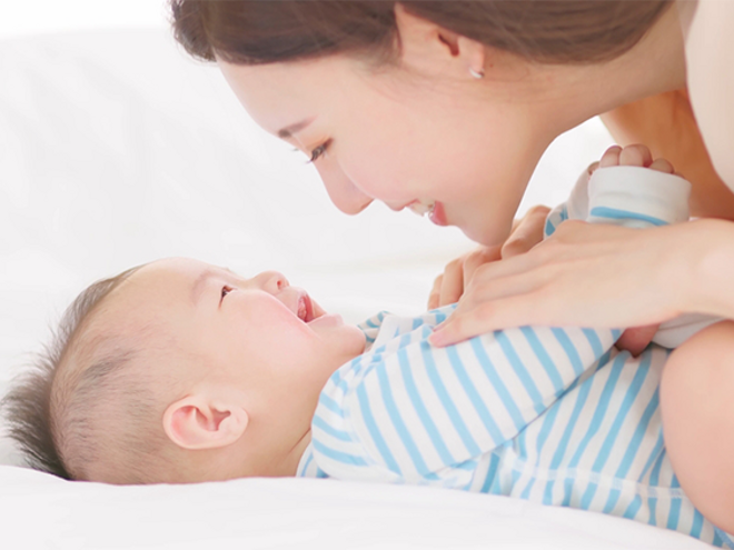 Young Asian mother plays with her happy baby on the bed.