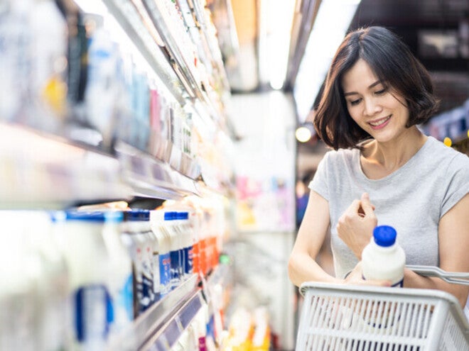 Young Asian woman putting a milk bottle in her basket after choosing from the types of milk in the supermarket
