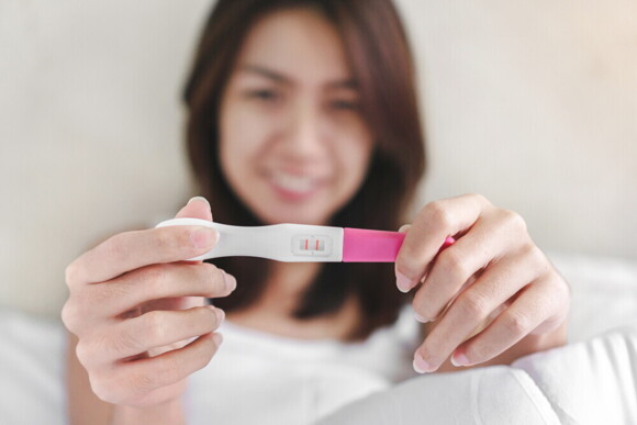 Asian woman flashing pink pregnancy test.