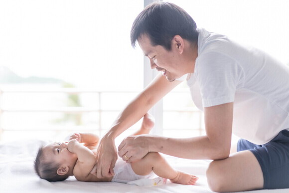 Young Filipino dad smiles as he changes his baby's diaper.
