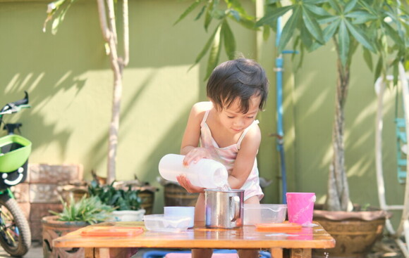 Article_Image-2 Filipino toddler pours water into a metal cup for a family activity.