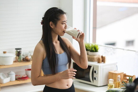Young Filipina in fitness wear drinks a glass of milk.