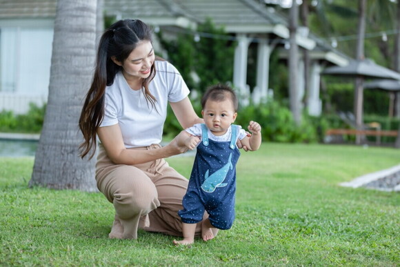 Article_Image-1 Filipino mom holds her baby who is learning to walk at a park.