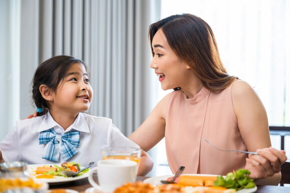 Article_Image-2 Asian moms talks to her school-age daughter while eating at home.